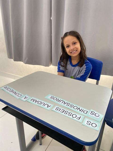 Aluna sorrindo na carteira durante atividade sobre fósseis