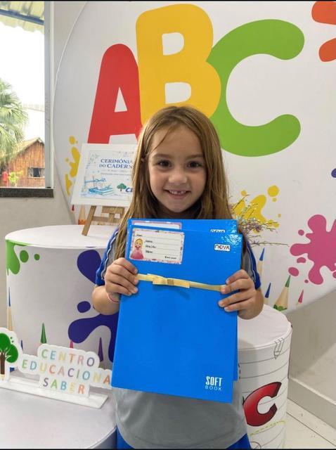 Aluna mostrando seu caderno na sala decorada com letras ABC