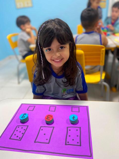 Aluna sorrindo em atividade de matemática com tampinhas coloridas